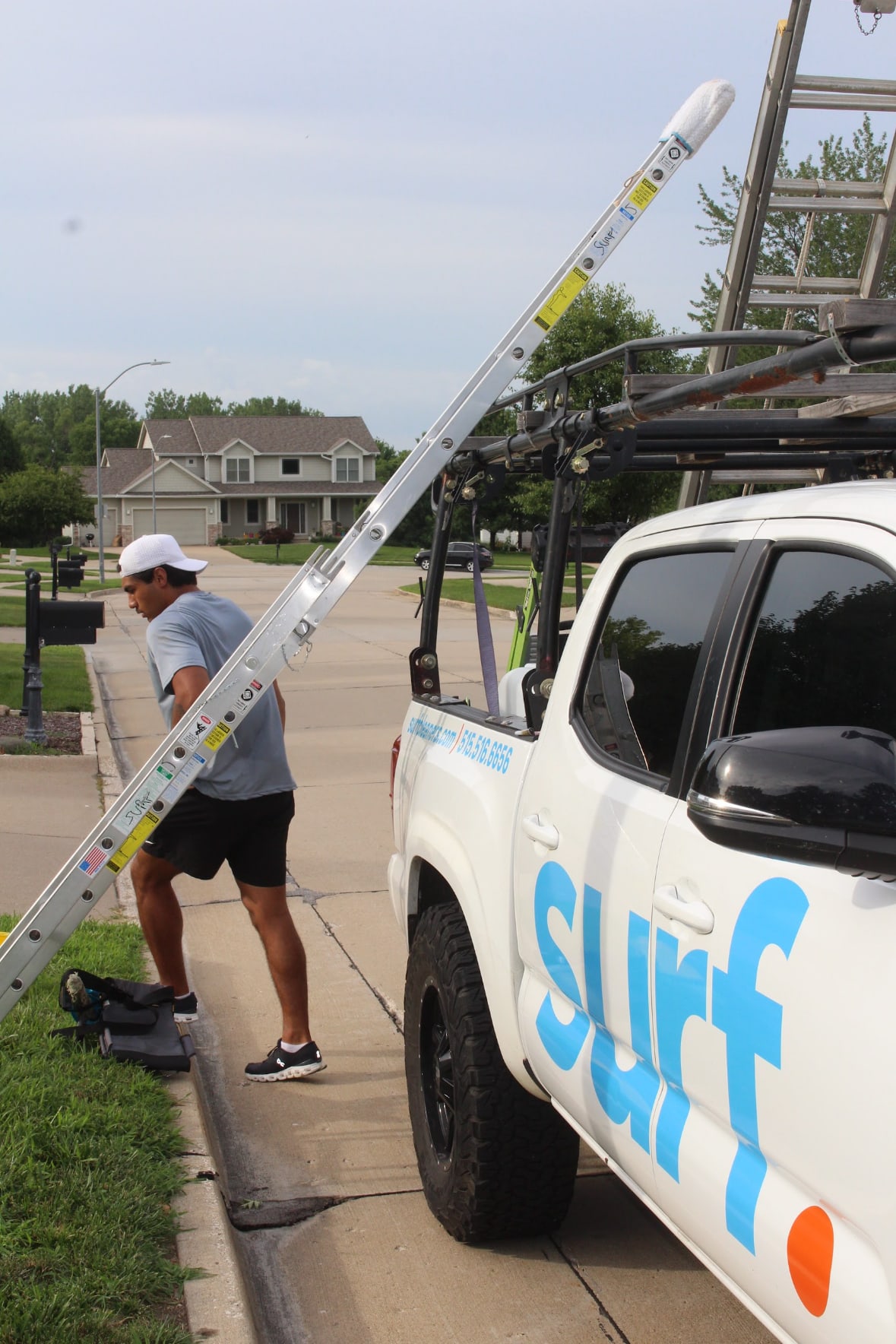 surf. technician carrying a ladder past the branded truck on a neighborhood job